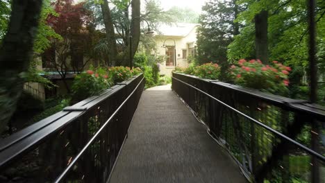 Fast-tracking-shot-of-wooden-bridge-with-flowers-in-the-forest-leading-to-a-cottage