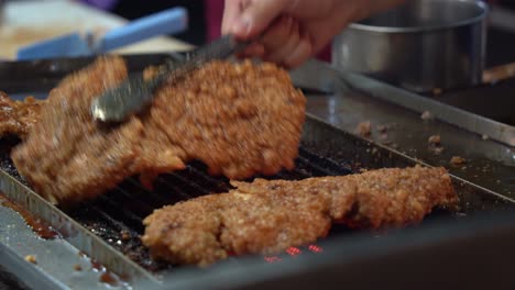 Crispy-honey-soy-coated-delicious-fried-chicken-fillet-grilling-on-hot-grill,-professional-chef-flip-side-with-a-pair-of-tongs-at-famous-night-market,-Taiwan,-Asia