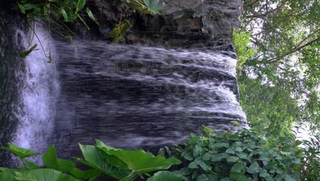Vertical-video---Water-cascade-on-rocks,-waterfall-surrounded-by-lush-vegetation