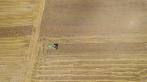 Harvesting-Mowing-Tractor-Machine-Working-Moving-on-Agricultural-Dry-Golden-Soil-in-Countryside-Farm-Land,-Rural-Landscape-and-Farming,-Aerial-Top-Down-View