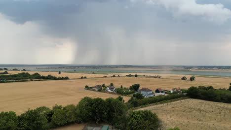 Aerial-footage-of-harvested-fields-with-rain-clouds-and-rain-burst-in-the-distance,-drone-dolly-left-to-right
