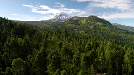 Backwards-drone-shot-showing-the-snowy-top-of-the-popocatepetl-volcano-in-mexico-city-and-the-lush-forests-that-surround-it