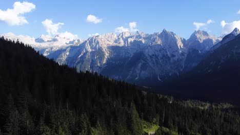 Toma-De-Un-Dron-De-4k-De-Un-Bosque-Lleno-De-Pinos-Con-Montañas-Sobresalientes-Y-Formaciones-Rocosas-En-El-Fondo-En-La-Hermosa-Zona-De-Los-Dolomitas-En-El-Norte-De-Italia