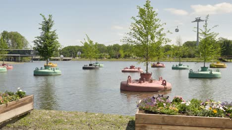 Panoramic-shot-of-trees-growing-in-metal-containers-floating-in-a-park-pond-with-a-moving-cable-cars-in-the-background