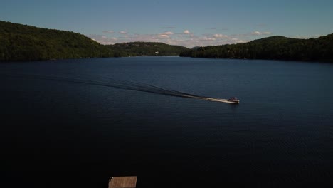 Aerial-shot-of-boat-passing-by-and-creating-waves-on-a-lake,-summer-day
