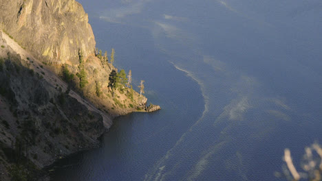Static-shot-looking-down-at-the-crystal-blue-water-in-Crater-Lake-Oregon-with-the-steep-mountain-ridge-meeting-the-water-line