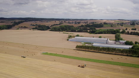 Up-drone-aerial-shot-over-wide-filed-during-harvesting-in-Poland---tractor-and-people-working-with-straw-cubes