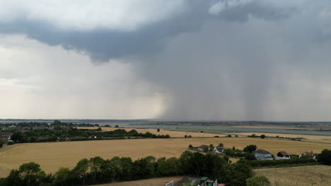 Aerial-footage-of-dry-summer-fields,-with-large-storm-cell-in-the-distance-with-rain-being-released,-drone-forward-motion