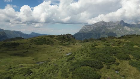 El-Dron-Pasa-Sobre-Un-Pequeño-Monte-En-Los-Alpes-Suizos,-Cielo-Nublado-Y-Altas-Montañas-Detrás,-Obwalden,-Engelberg