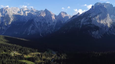 Rotational-aerial-4K-drone-shot-of-a-beautiful-valley-in-the-Dolomites,-full-of-pine-trees-with-an-outstanding-view-of-mountains-and-rock-formations-in-the-background-in-North-Italy