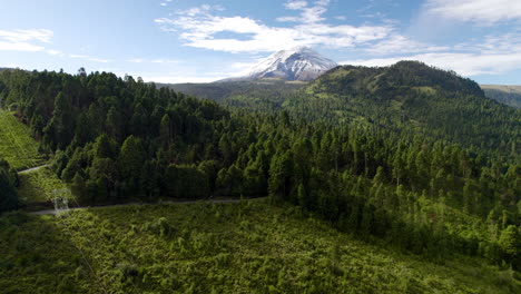 Backwards-drone-shot-dronie-type-showing-the-snowy-top-of-the-popocatepetl-volcano-in-mexico-city-and-the-lush-forests-that-surround-it