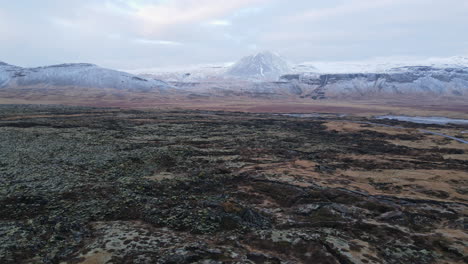 Toma-Aérea-De-Un-Campo-De-Lava-Frente-A-Las-Montañas-En-Islandia