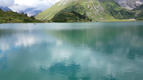 Calm-water-of-an-alpine-lake-with-reflection-of-sky-clouds-and-Swiss-mountains-behind,-aerial-drone-view,-Obwalden,-Engelberg