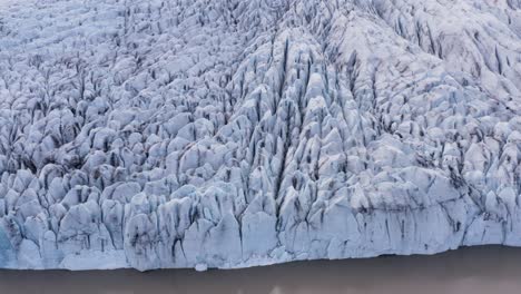 Face-of-Fjallsárlón-white-ice-glacier-with-brown-water-lagoon,-aerial