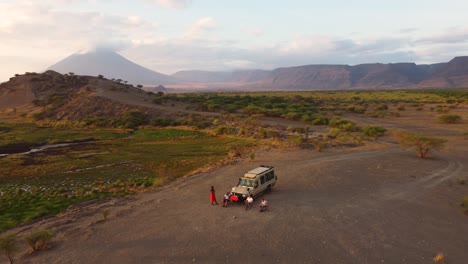 An-amazing-drone-shot-of-a-safari-jeep-parked-on-a-hilltop-with-people-sitting-outside-and-enjoying-the-sunrise-view-of-Lake-Natron-and-Ol-Doinyo-Lengai-volcano-in-the-background-in-Tanzania-in-Africa