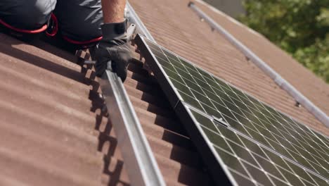 Mounting-new-installed-solar-panel-on-rails,-closeup-of-worker-on-roof,-day