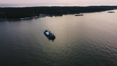 Cinematic-aerial-drone-shot-of-a-ferry-moving-across-the-river-with-a-lot-of-people-traveling-across