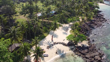 A-beautiful-drone-shot-of-the-tropical-island-of-Koh-Kood-flying-over-Koh-Kood-Beach-Resort-and-a-small-and-charming-beach-surrounded-by-palm-trees,-in-Thailand-in-Southeast-Asia