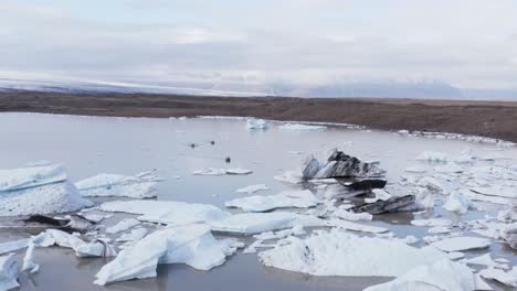 Tourist-in-three-small-boats-visiting-icebergs-floating-in-glacial-lagoon,-aerial
