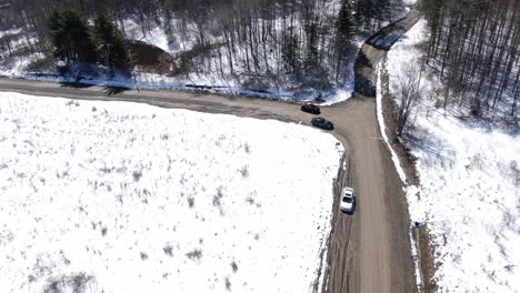 Imágenes-Aéreas-De-Drones-Siguiendo-A-Un-Camión-Negro-Conduciendo-Por-Un-Camino-De-Tierra-En-Un-Bosque-Cubierto-De-Nieve