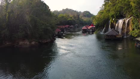Eine-Wunderbare-Rotierende-4k-drohnenaufnahme-Aus-Der-Luft-Eines-Flusses-Im-Dschungel-Von-Thailand,-Mit-Blick-Auf-Ein-Kleines-Charmantes-Schwimmendes-Dorf-Und-Einen-Wunderschönen-Wasserfall-Im-Sai-Yok-Nationalpark-In-Asien