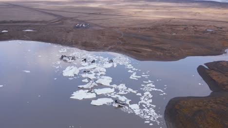 Icebergs-stuck-in-glacial-lagoon-at-river-mouth,-climate-change-impact,-aerial