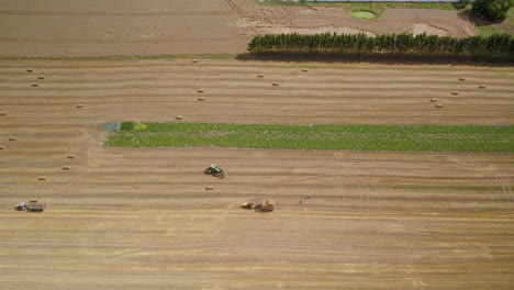 Tractors-work-in-the-field-to-collect-cut-grain-in-the-form-of-straw-cubes---aerial-drone-shot