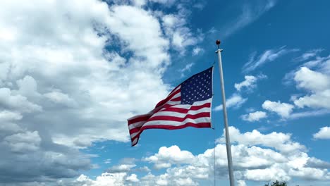 USA-American-flag-waves-against-bright-sunny-sky-with-white-puffy-clouds