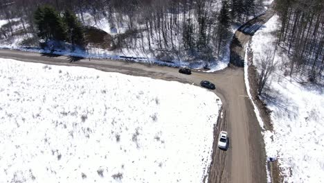 Aerial-Drone-Footage-Following-a-Black-Car-as-it-Drives-and-Turns-Down-a-Dirt-Road-in-the-Snow-Covered-Wilderness