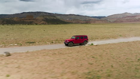 Red-Jeep-Wrangler-Driving-Fast-On-Dirt-Road-Through-Semi-arid-Desert-In-Utah,-USA