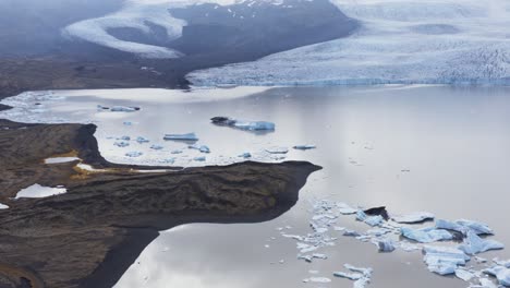 Shrinking-glacier-of-Fjallsárlón-with-large-water-lagoon-and-icebergs,-aerial