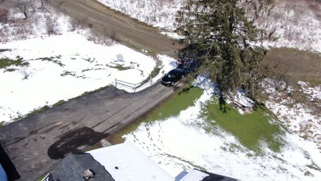 Aerial-Drone-Footage-of-a-Car-Backing-Down-the-Driveway-of-an-Old,-White-House-on-a-Sunny,-Snowy-Day
