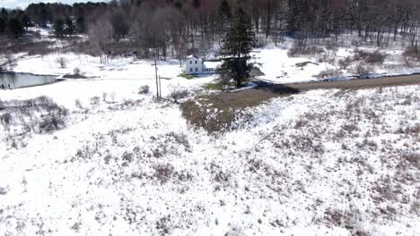 Aerial-Drone-Footage-Backing-Away-From-an-Old,-White-House-to-Reveal-the-Snow-Covered-Countryside