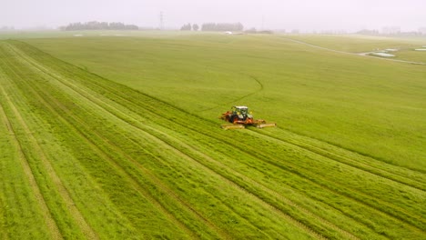 Farmer-on-Tractor-mowing-fresh-green-grass-for-hay-or-cattle-feed,-misty-day