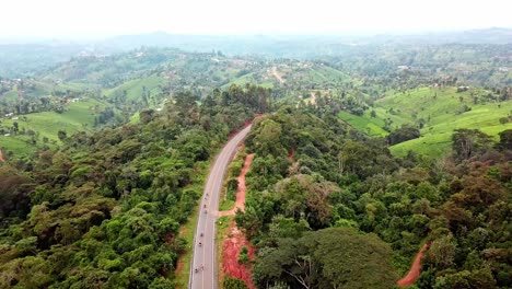 Impresionante-Vista-Aérea-De-La-Carretera-Asfaltada-En-Medio-De-La-Selva-Tropical-Con-Motocicletas-En-Las-Colinas-De-Chogoria,-Kenia,-áfrica