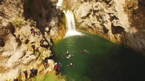 People-jumping-in-river,-waterfall-and-rocks-behind