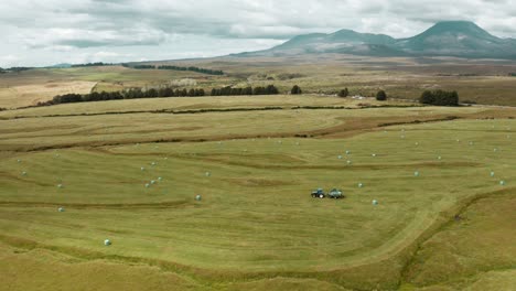 Tractor-creating-hay-bales-on-rural-green-grass-field,-agriculture-concept,-New-Zealand-countryside-landscape,-aerial