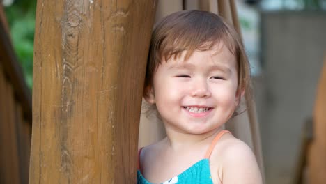 Portrait-of-cute-shy-2-year-old-girl-with-toothy-smile-at-outdoor-playground