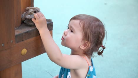 Face-close-up-of-beautiful-toddler-girl-stacking-stones-at-playground---slow-motion