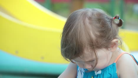 Upset-little-girl-toddler-sitting-on-the-floor-at-an-outdoor-playground-with-head-bent
