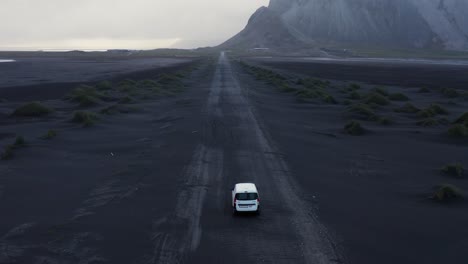 White-car-standing-on-long-straight-black-volcanic-sand-road-in-Iceland,-aerial