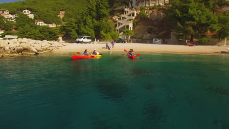 People-kayaking-in-sea-near-coast,-green-nature-and-rocks