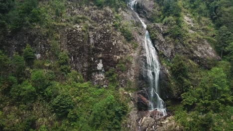 An-establishing-ascending-aerial-shot-of-a-waterfall-reveals-a-dam-at-the-top-of-the-mountain