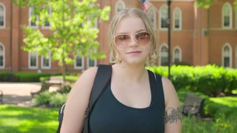 Girl-student-wearing-sunglasses-stands-in-from-of-a-college-university