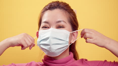 Close-up-Brunette-young-Asian-woman-happy-and-joyous-smiling-and-taking-off-the-protective-mask-for-fresh-air-after-the-CIVID-19-situation-unravels-with-the-yellow-background