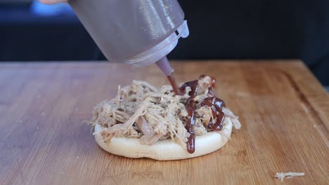 Pulled-Pork-Sandwich,-Das-In-Zeitlupe-Mit-Barbecue-Sauce-Beträufelt-Wird