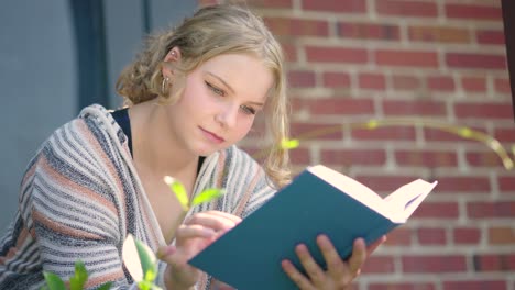 Close-up-of-girl-student-reading-a-book-outside-of-a-school-building