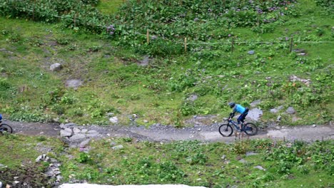Bikers-are-going-through-green-meadows-on-a-small-gravel-path,-Engelberg,-Obwalden