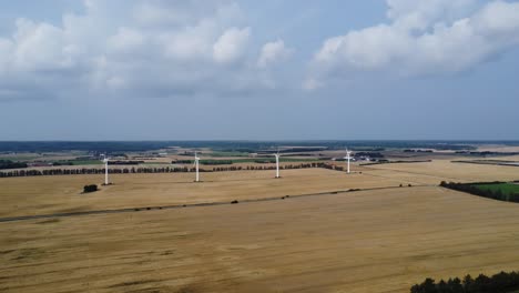 4-Windkraftanlagen-Auf-Einer-Wiese-Mit-Schönen-Wolken-Am-Himmel-Im-Hintergrund,-Droneshot