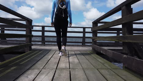Cinematic-shot-of-a-woman-walking-on-a-lagoon-pier-and-raising-her-arms-in-joy-at-the-end